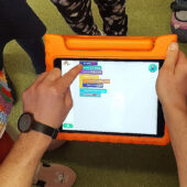 Mann hält Tablet. Kinder schauen zu.