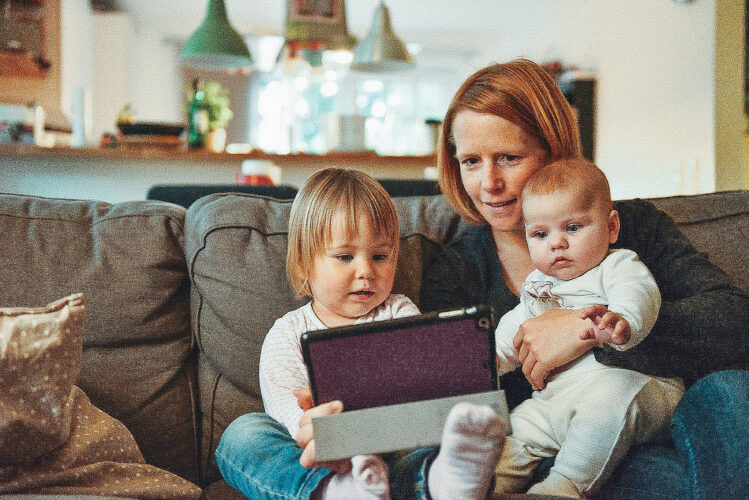 Mutter sitzt mit Kindern auf der Couch und schaut auf das Tablet.